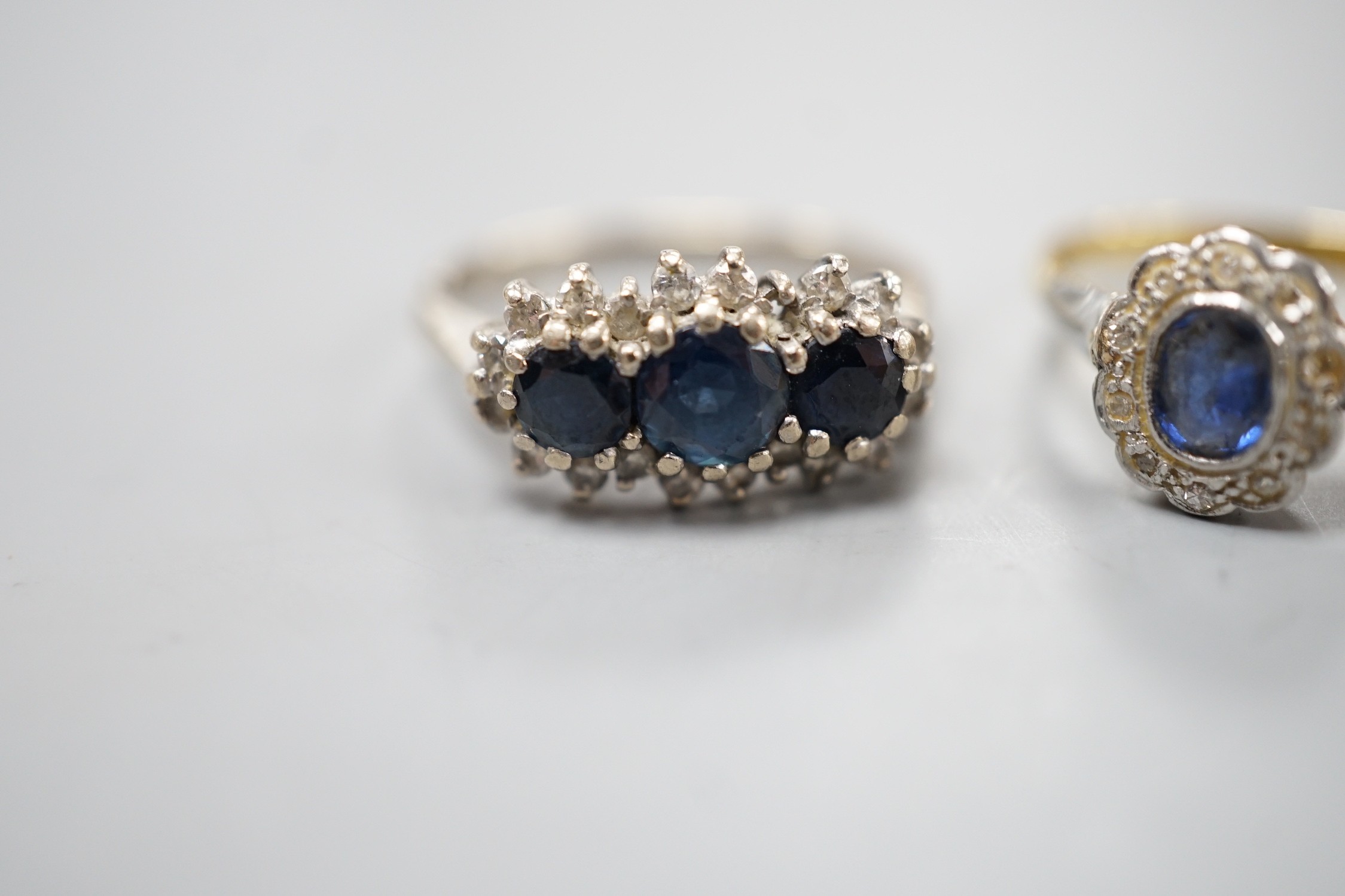 An 18ct white metal, sapphire and diamond set triple cluster ring, size O and a yellow metal, sapphire and diamond set oval cluster ring, size O/P, gross weight 6.8 grams.